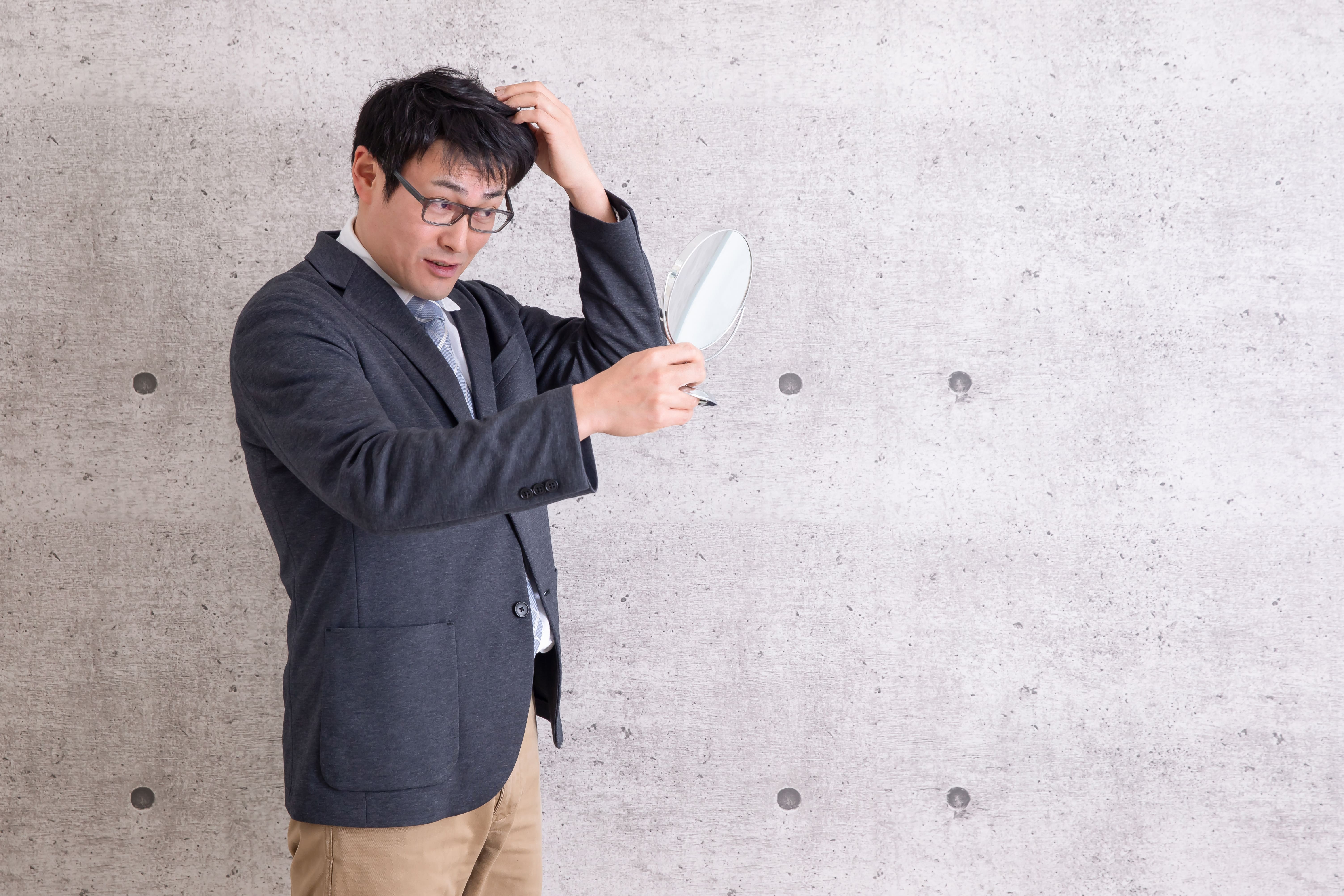 鏡を見ながら髪型を気にするスーツ姿の男性