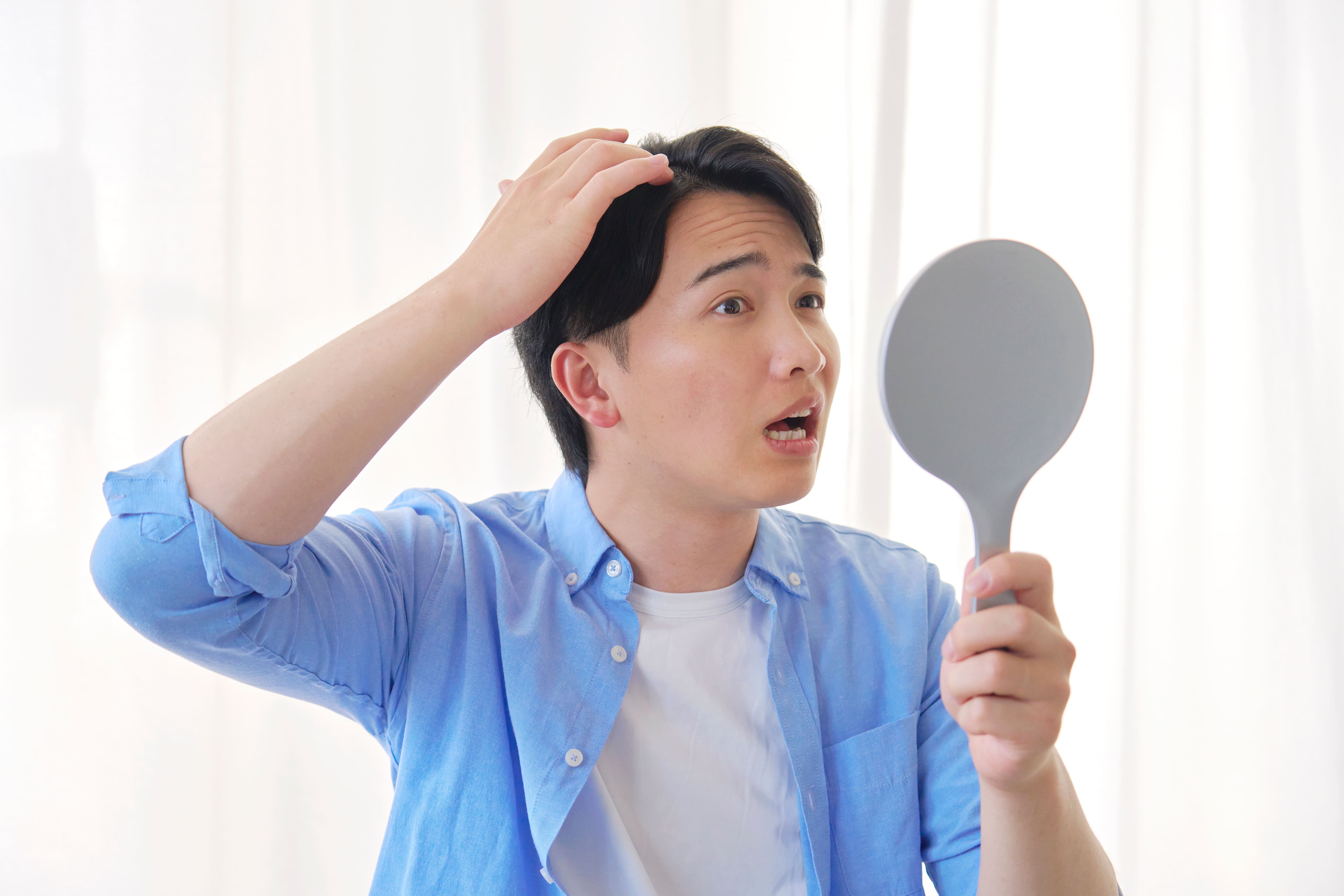 手鏡を見ながら髪の状態に驚く男性