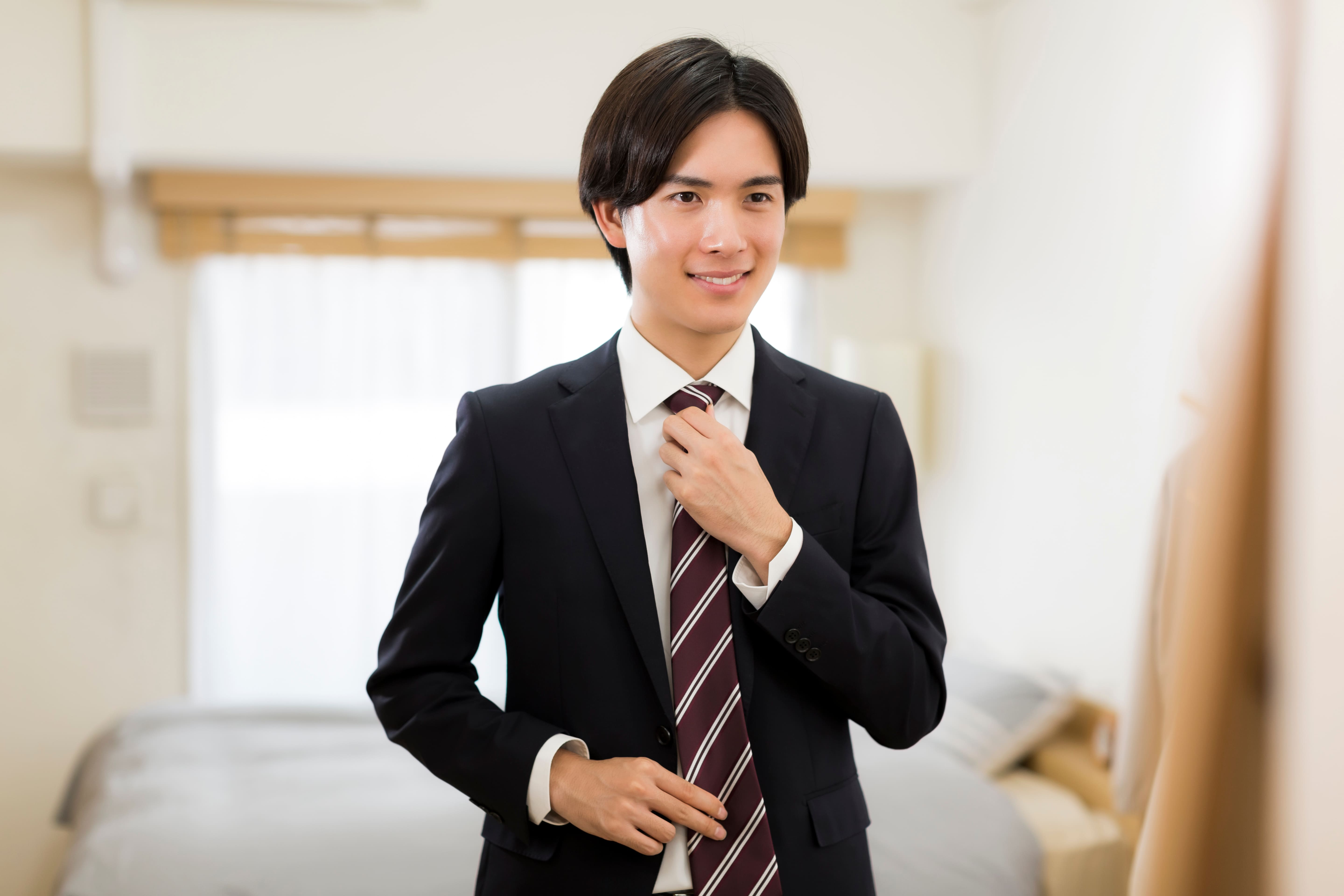 鏡の前でネクタイを整えるスーツ姿の男性