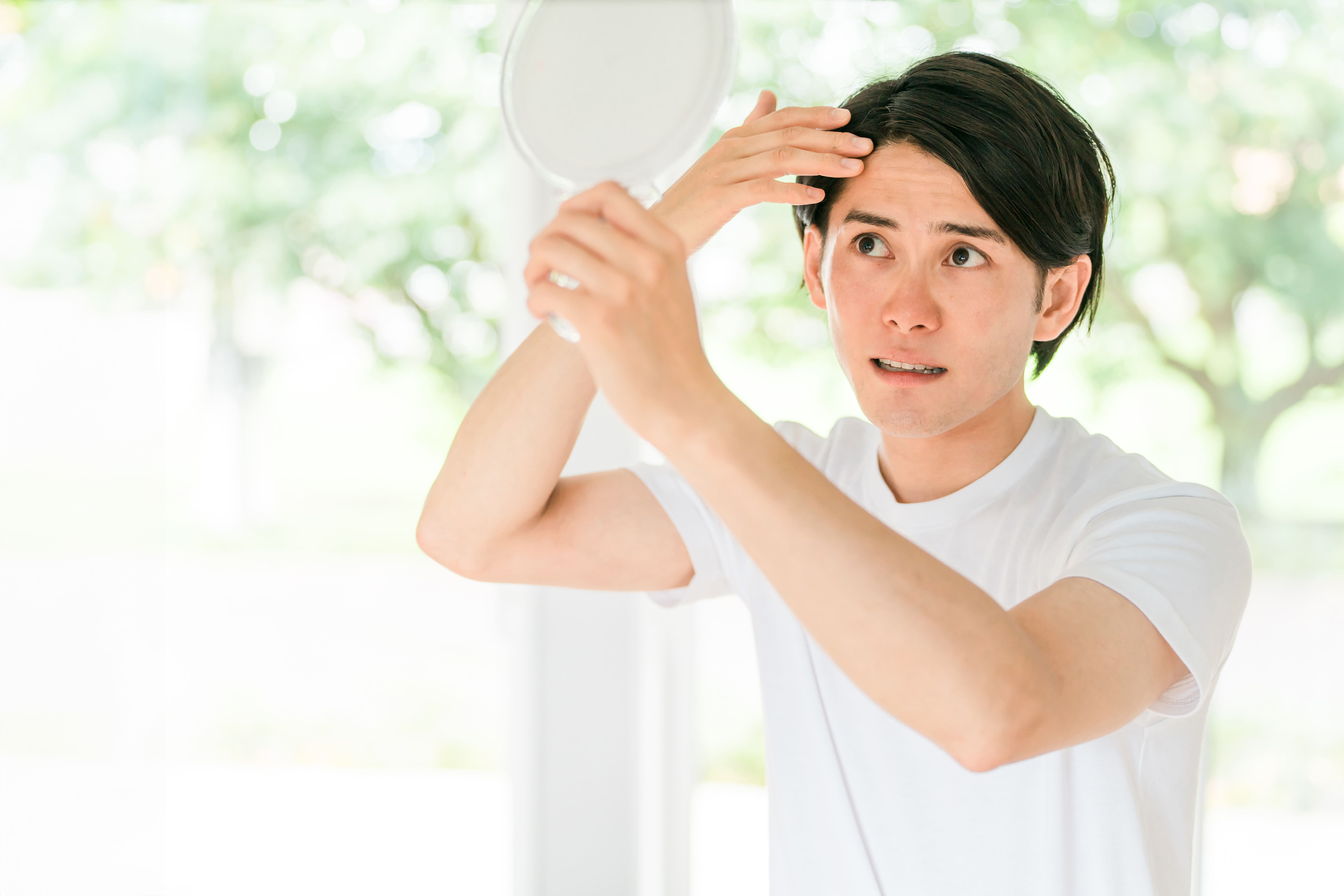 手鏡を見ながら前髪の生え際を気にする男性