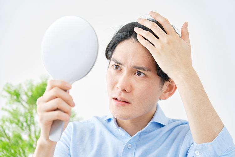 自宅でハンドミラーを持って髪の毛を見る男性