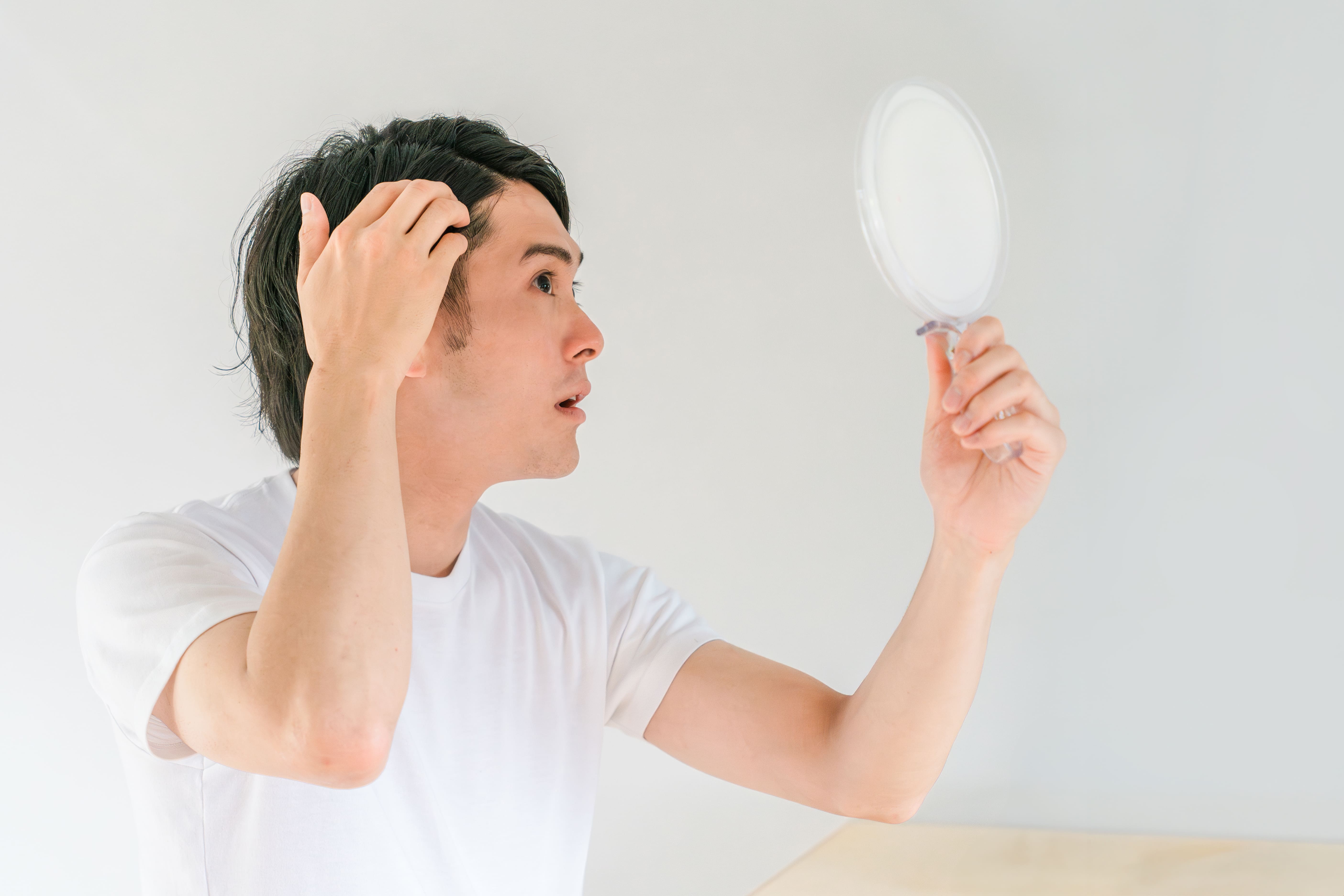 鏡を使って生え際の髪の状態を確認する男性