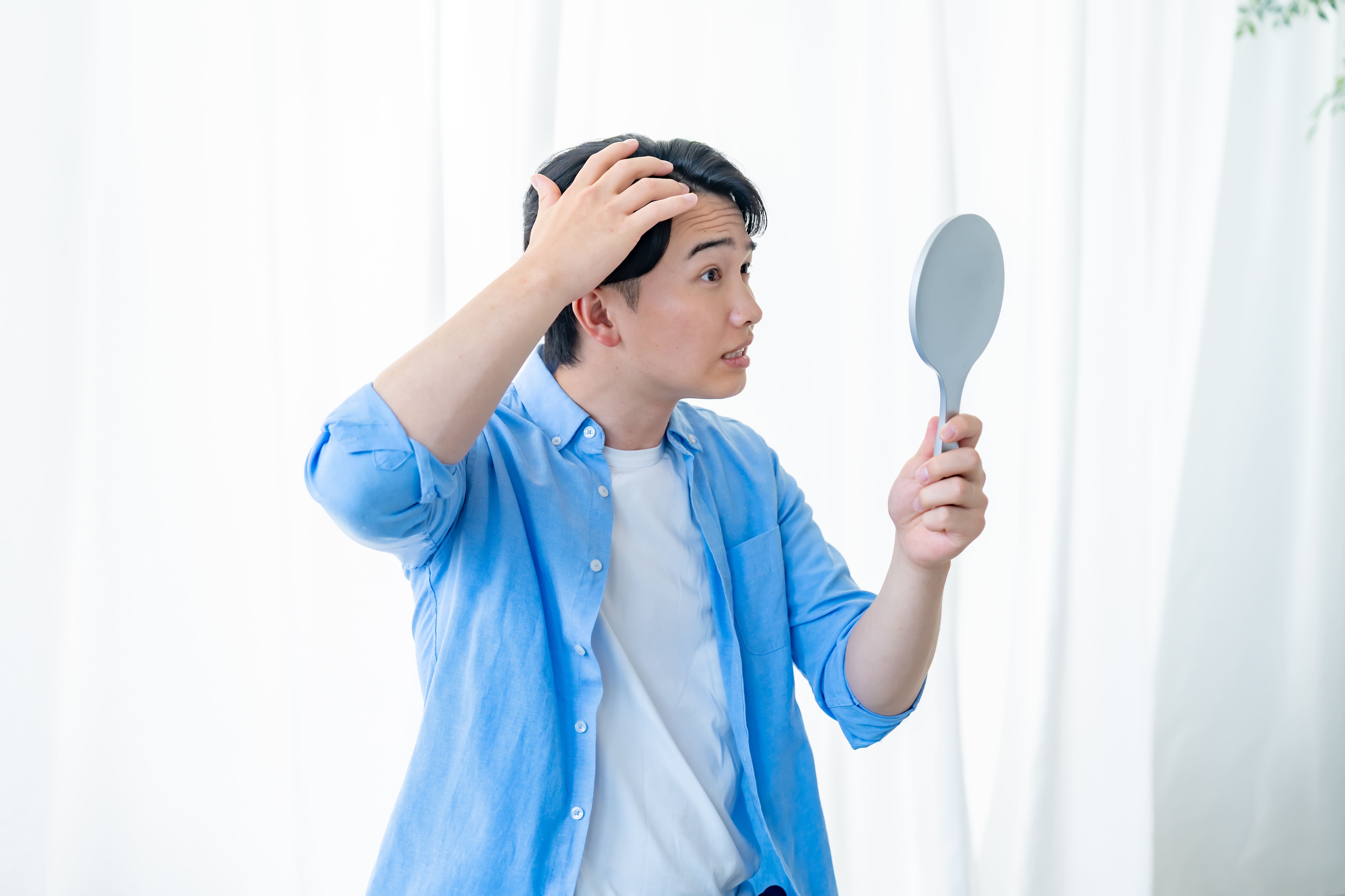 鏡を見ながら生え際や髪の状態を確認する男性