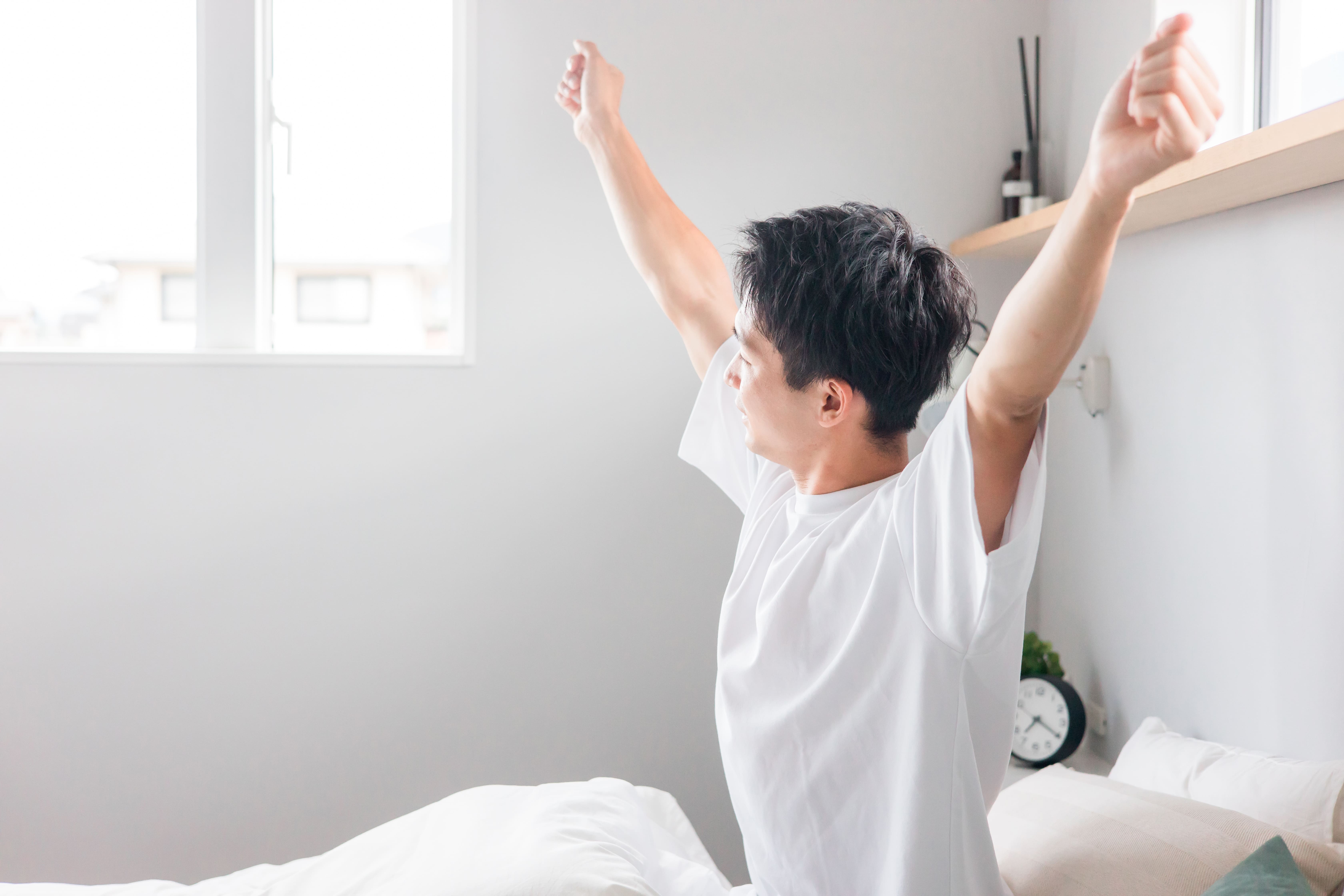 ベッドの上で両腕を伸ばして伸びをする男性