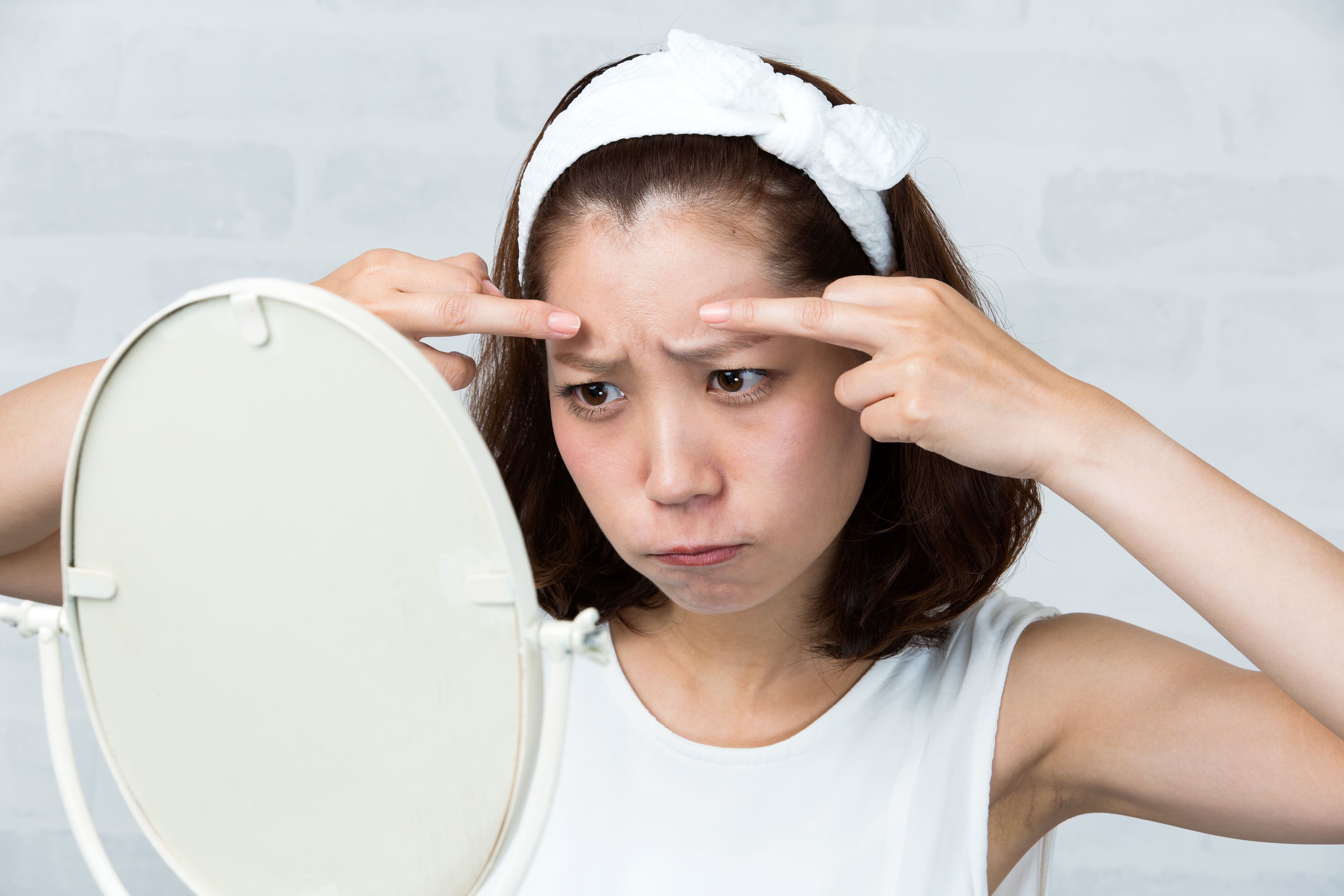 鏡を見ながら眉間のシワを気にする女性