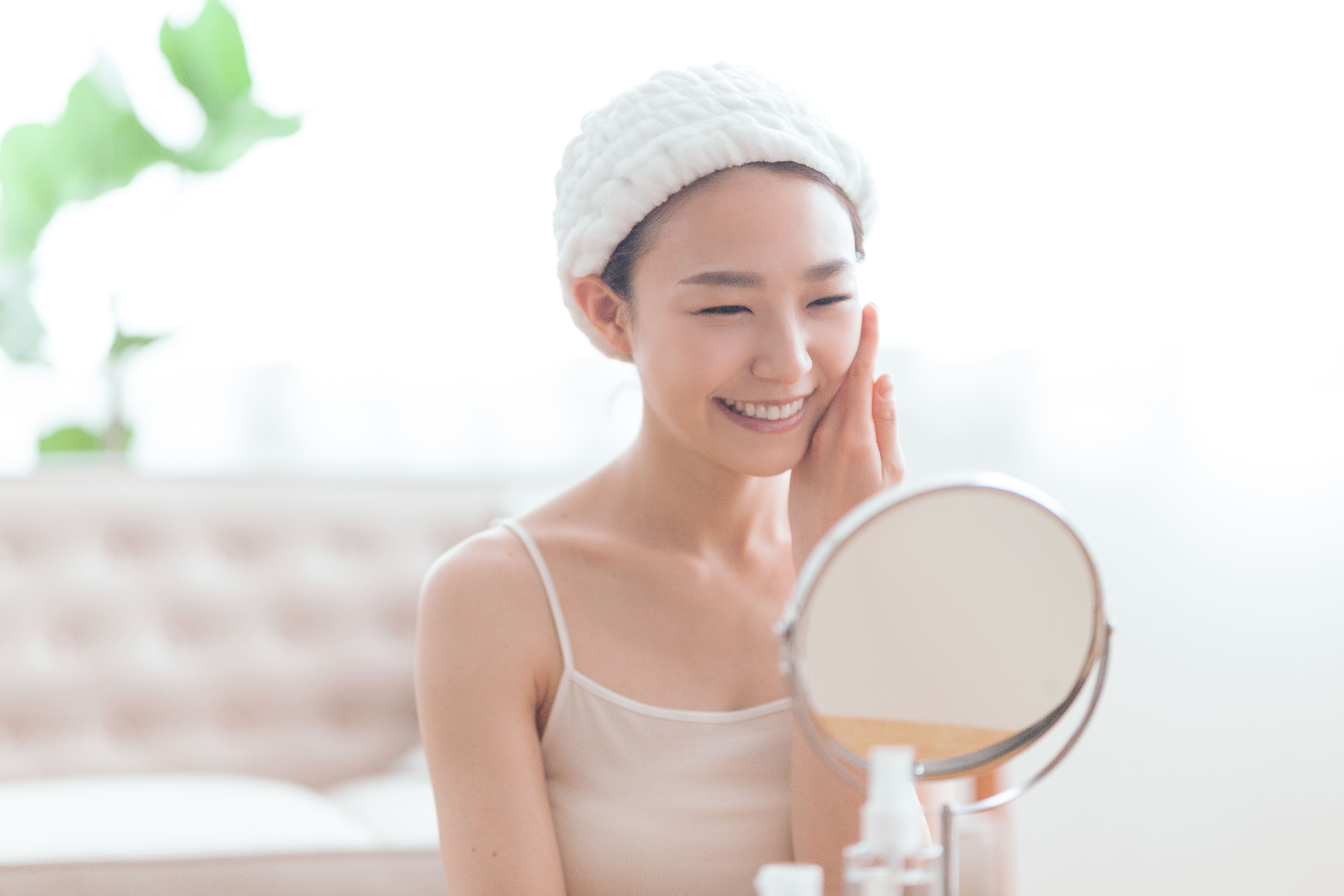 鏡を見ながら肌や顔の状態に満足する女性