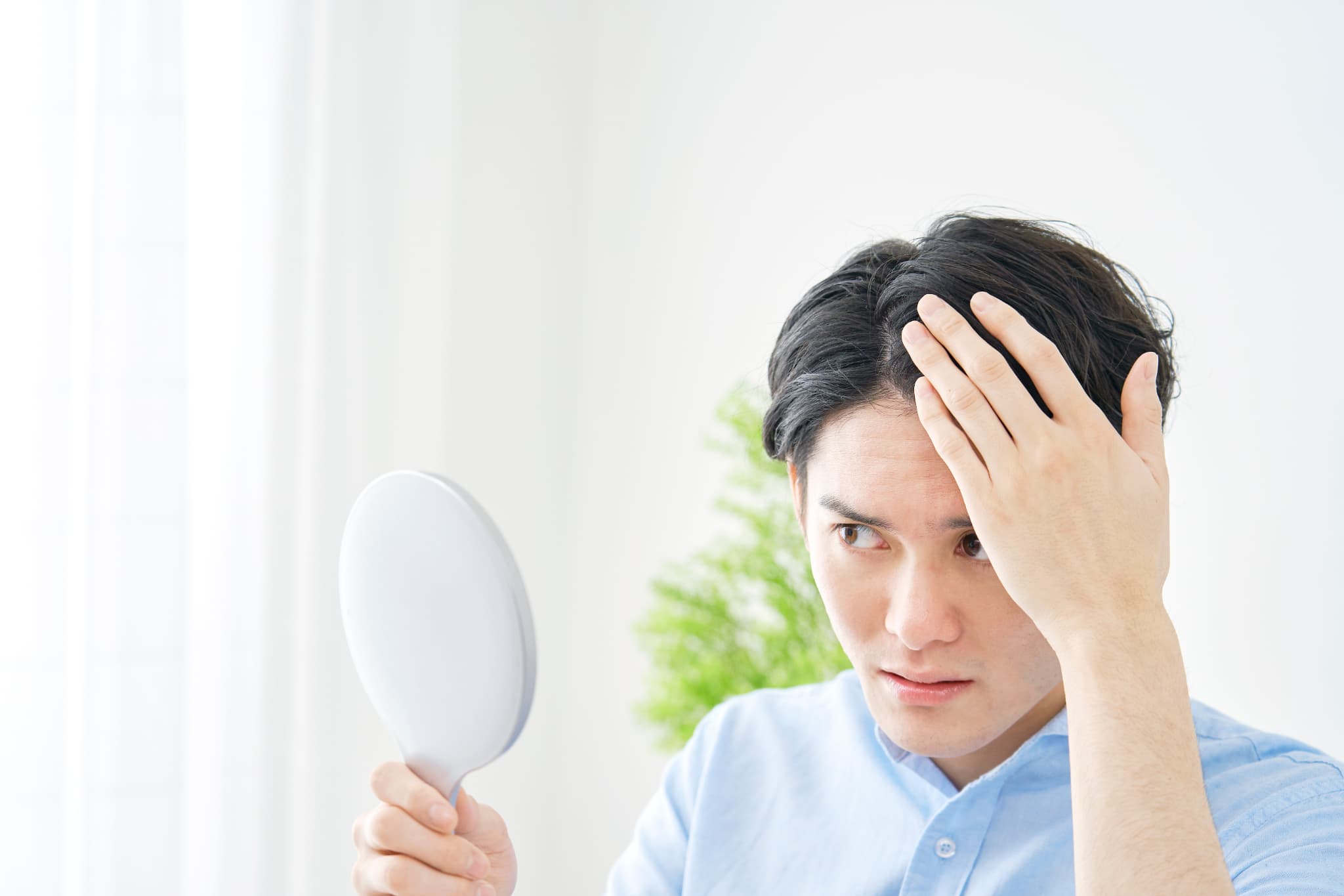 手鏡を見ながら生え際の髪の状態を確認している男性