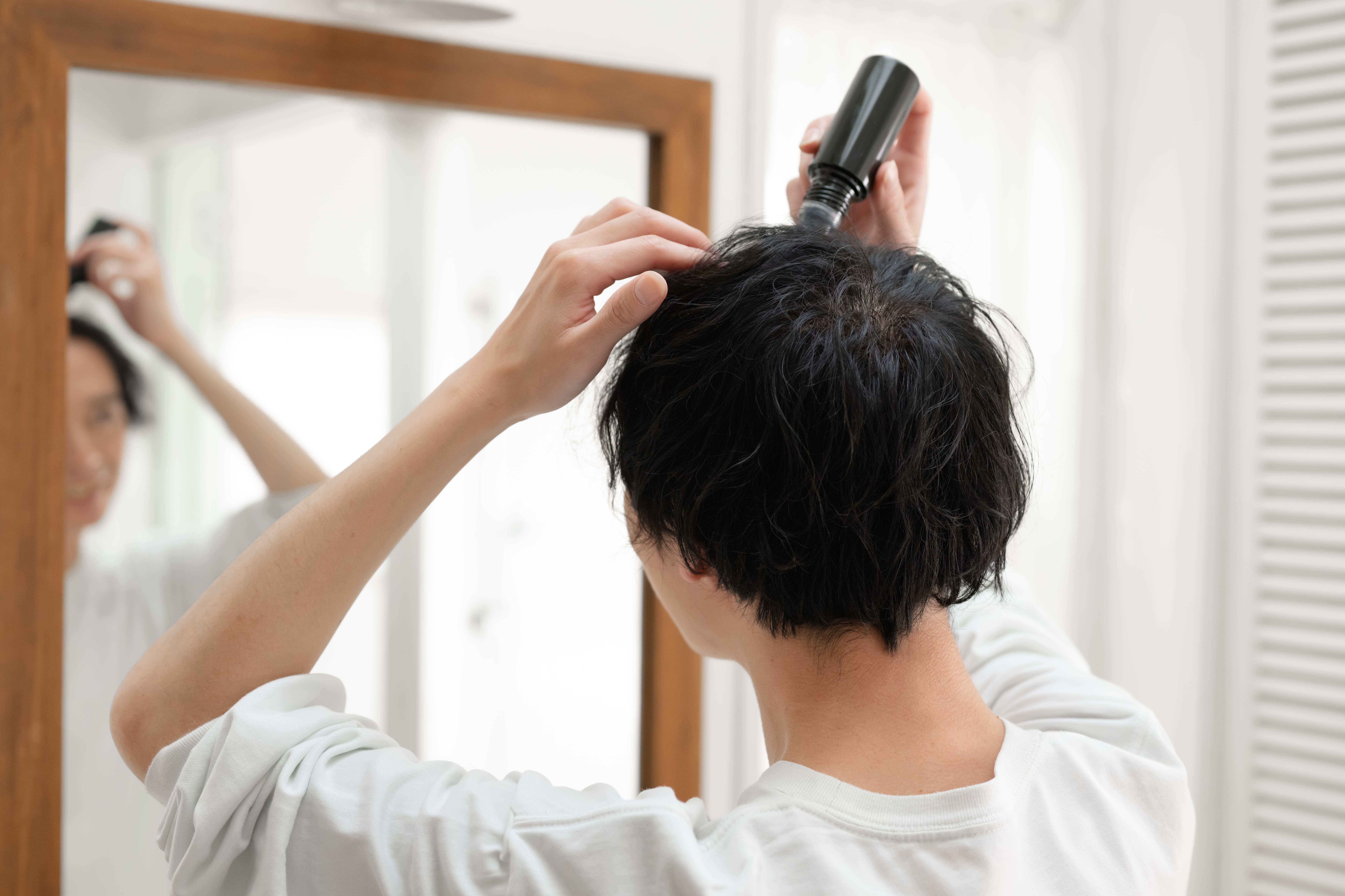 鏡を見ながら頭頂部に育毛剤を塗布する男性