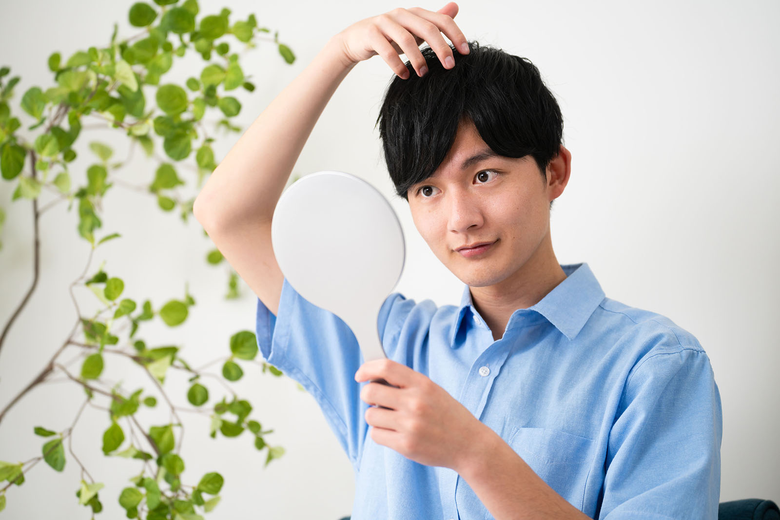 手鏡を見ながら髪の毛の状態を確認する男性
